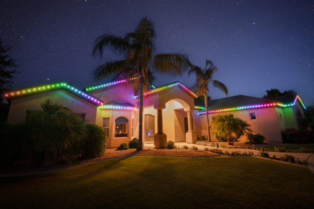 Brick house with red and blue holiday lights, lit walkway, and landscaped yard at dusk.