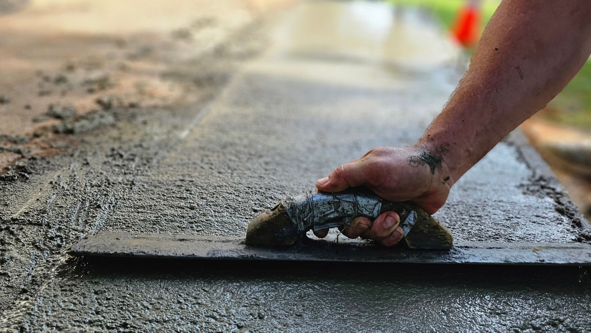 A person is using a trowel to spread concrete on a sidewalk.