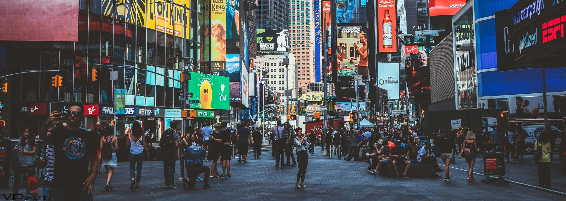 Busy neon-lit city street at dusk with crowds, taxis, and bright billboards in Times Square