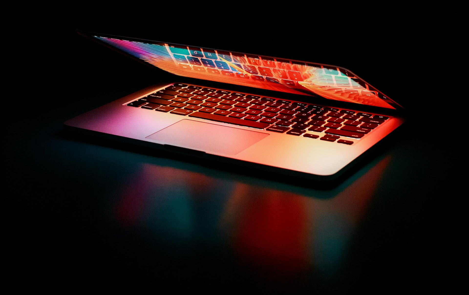 Open laptop glowing with red and pink light on a dark background