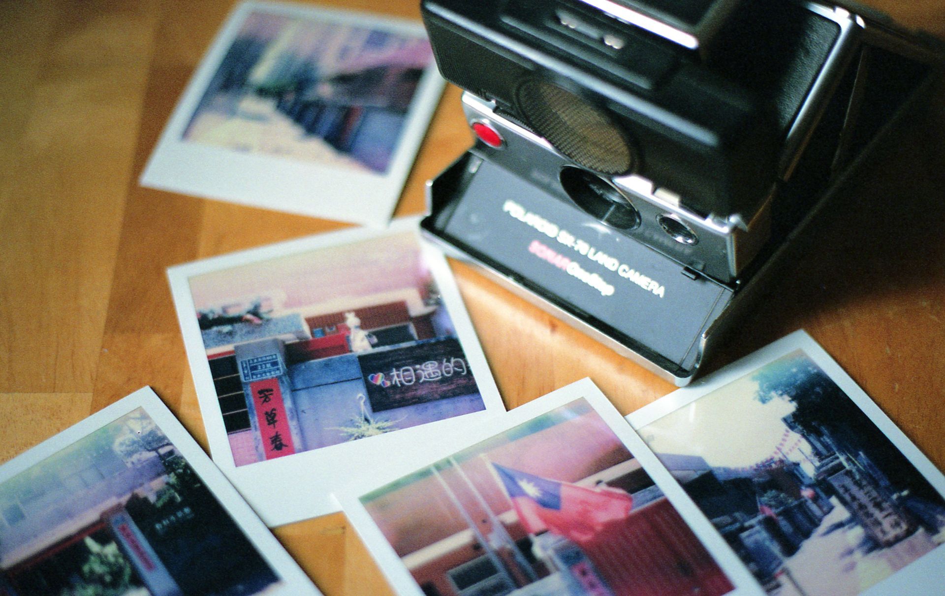 Scattered instant photos beside a black instant camera on a wooden table