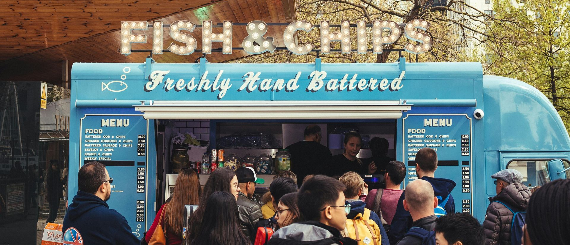 Blue fish and chips stall with a crowd ordering under a 
