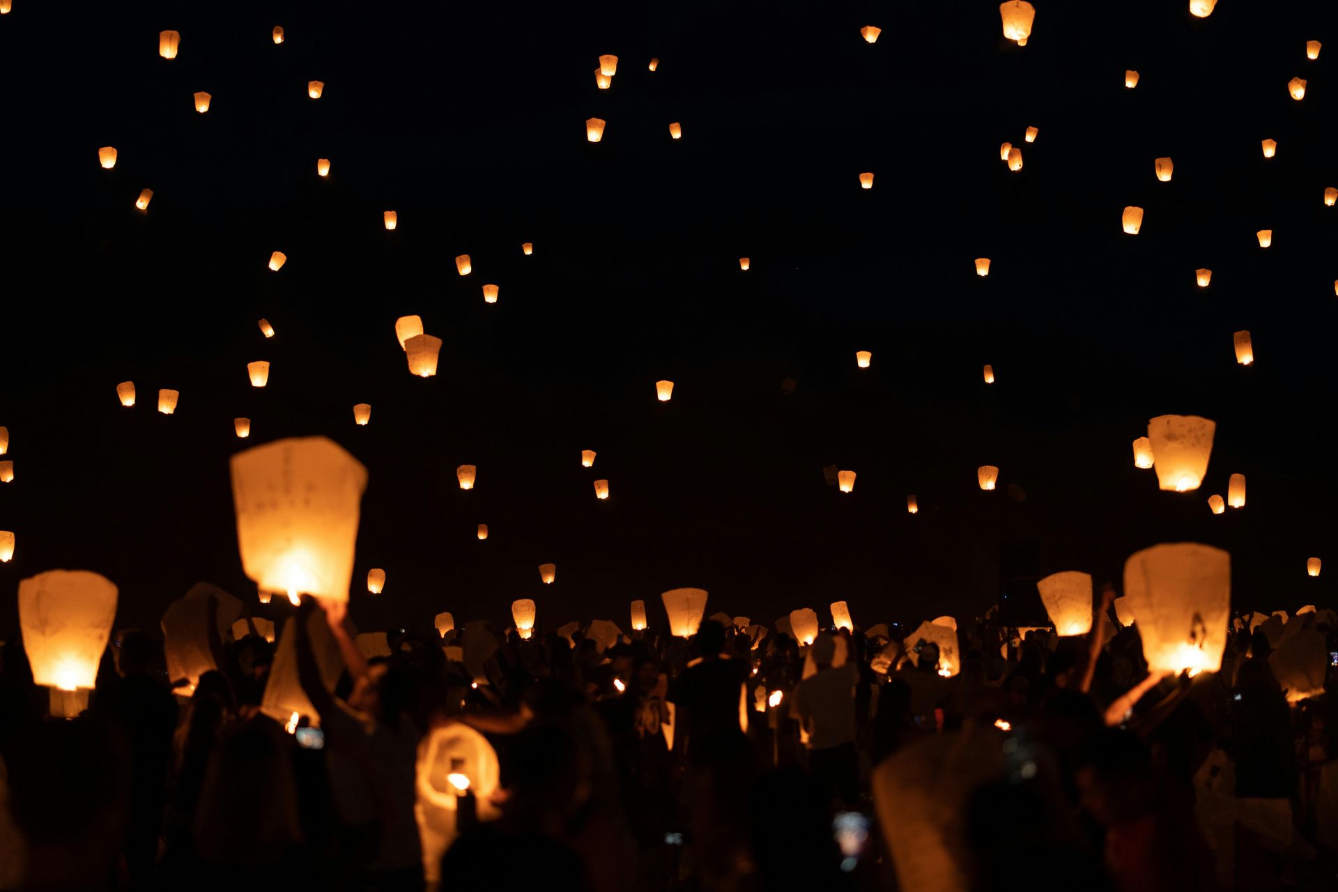 Night sky filled with glowing lanterns over a crowd releasing sky lanterns at a festival