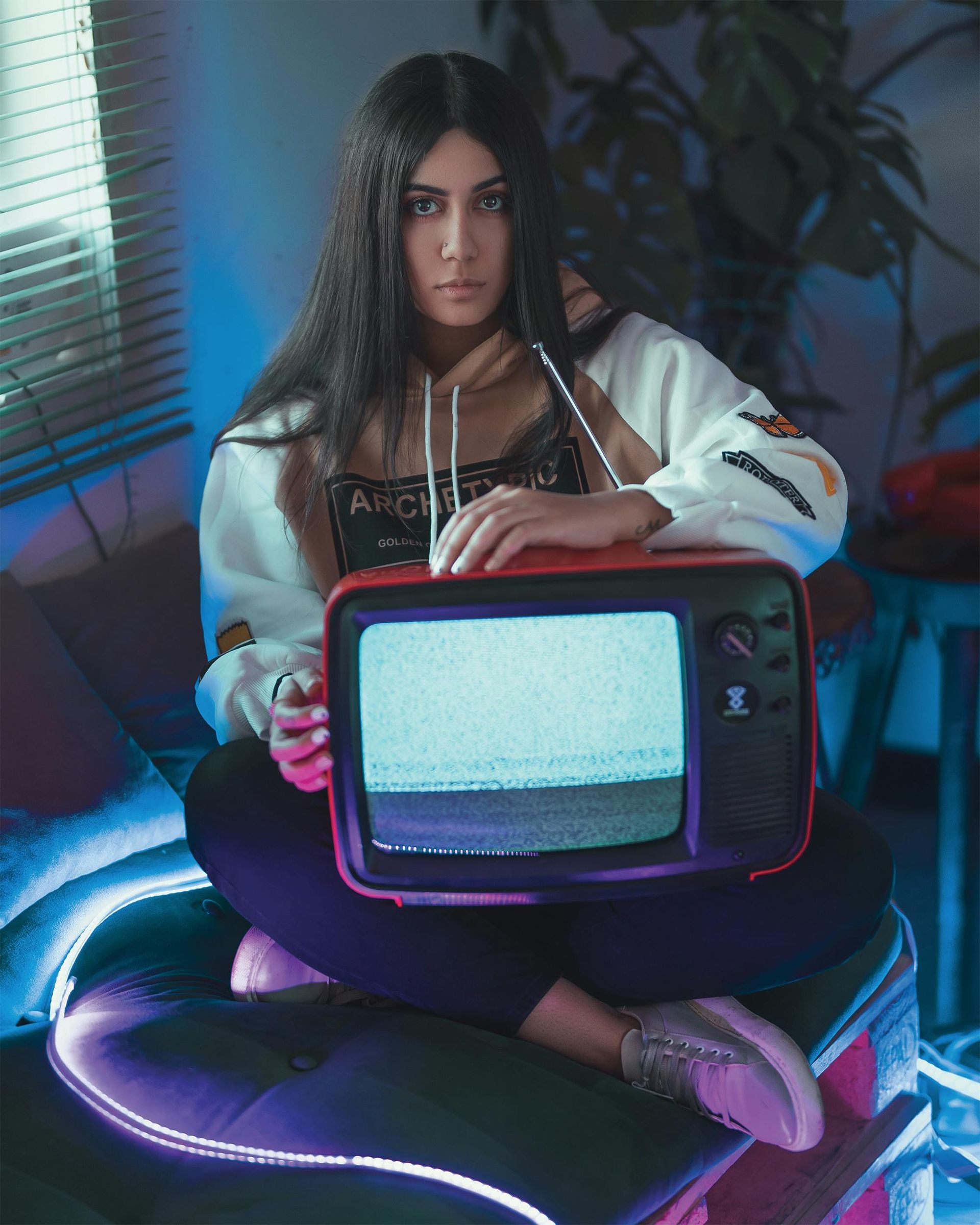 Person seated on a glowing chair holding a retro TV with static in a neon-lit room