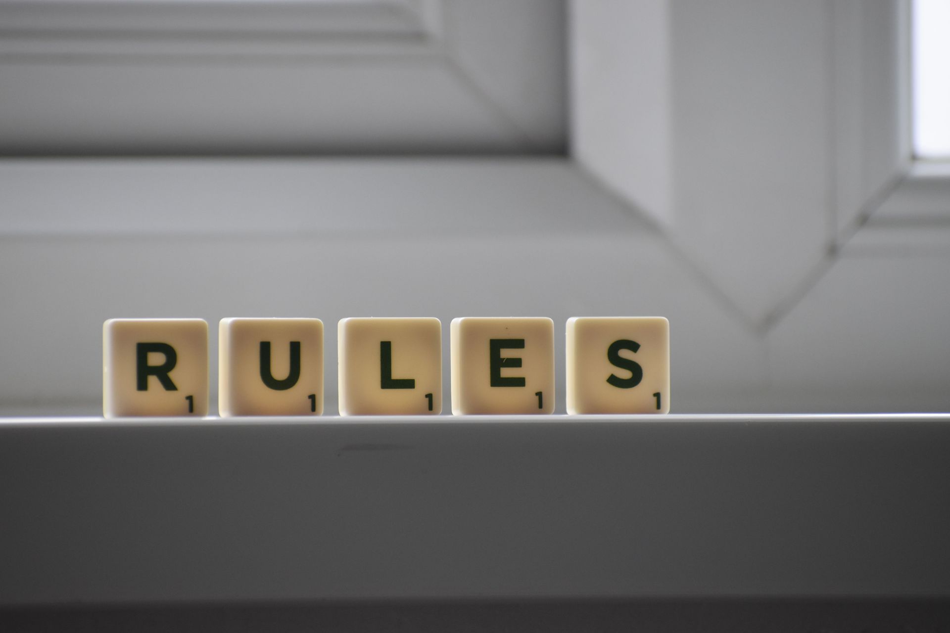 Wooden letter blocks spelling “RULES” on a windowsill with a blurred window background