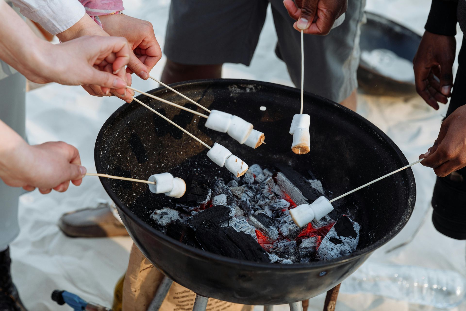 People roasting marshmallows over a small charcoal fire in a black fire pit