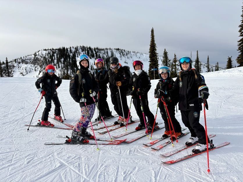 Kimberley Alpine Team Group of skiers in black outfits and colorful helmets posing on a snowy mountain slope