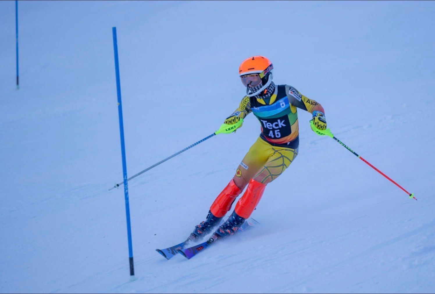 Kimberley Alpine Team Skier in orange helmet and red pants slaloms past a blue gate on a snowy course
