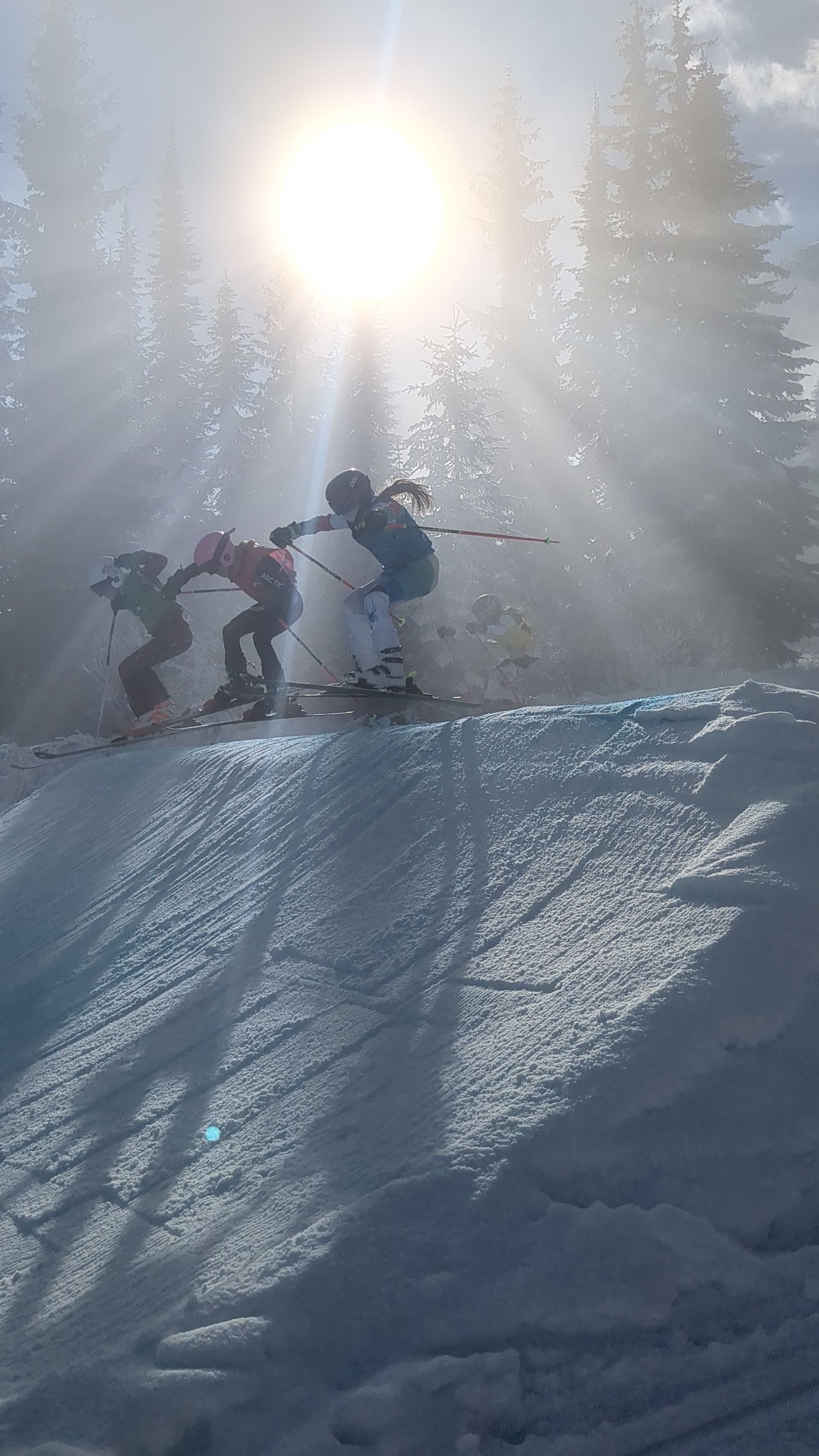 Kimberley Alpine Team Skiers on a snowy slope in bright sun, with sparkling snow and tall trees in the background