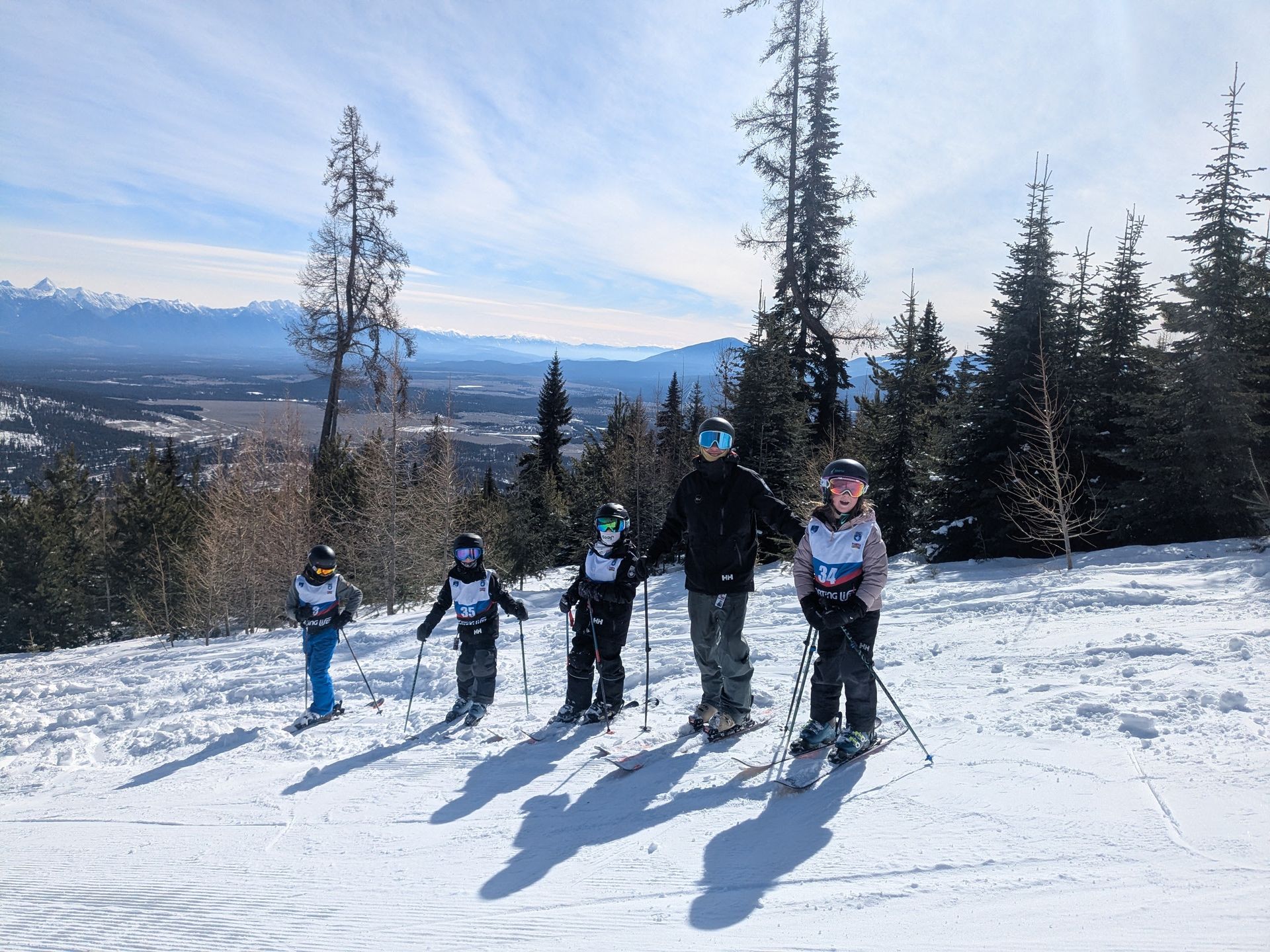 Kimberley Alpine Team Five skiers standing on a snowy slope with a mountain valley view in the background
