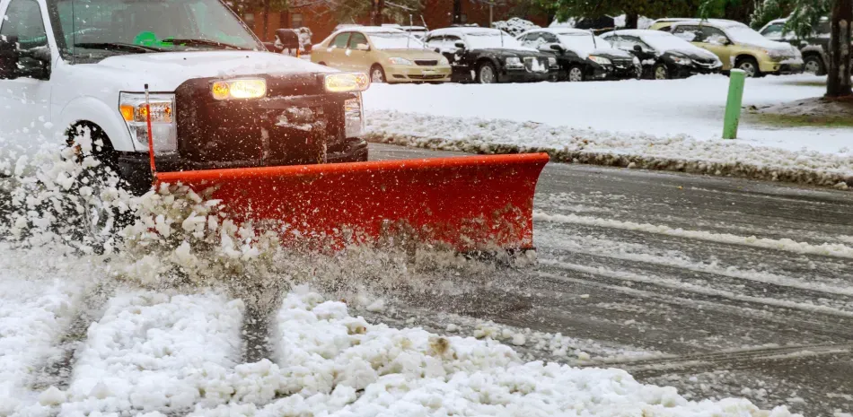 A snow plow is driving down a snowy street.