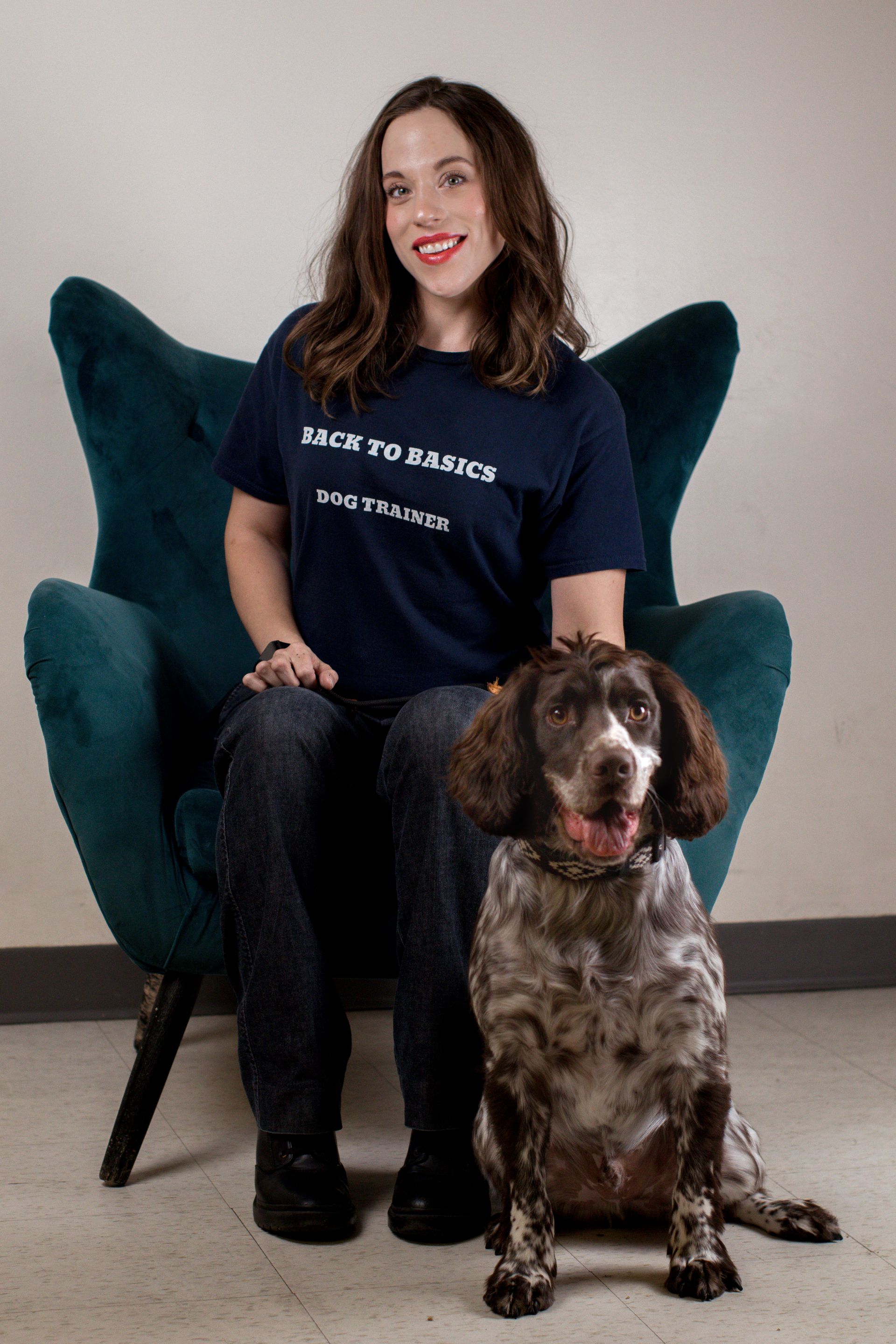 Woman in blue shirt seated in a teal chair, dog with brown spots sits beside her.