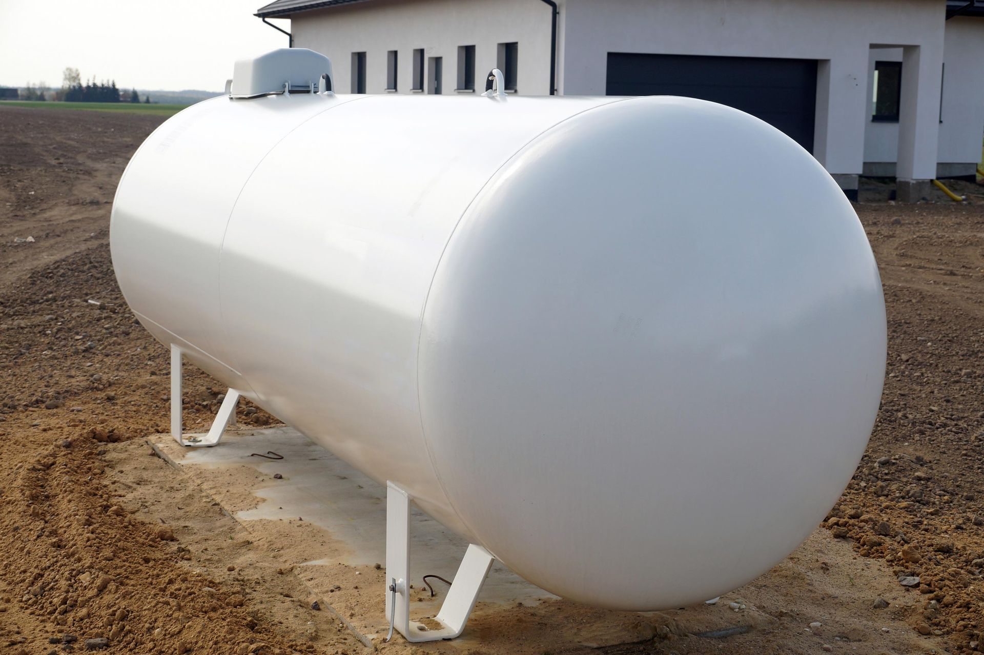 White cylindrical propane tank on metal legs outdoors near a building.