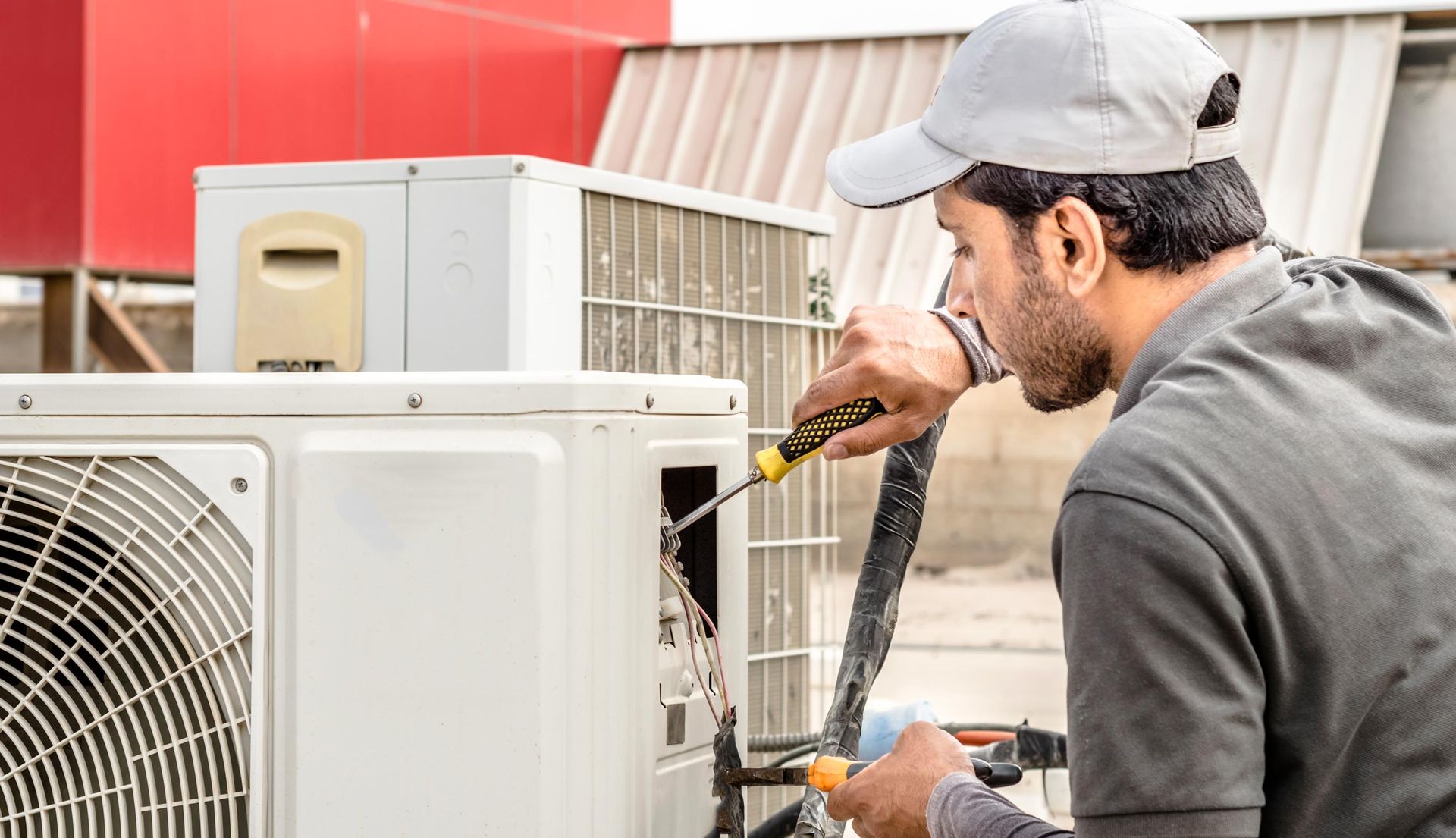 HVAC technician repairs an air conditioning unit outside, using a screwdriver.