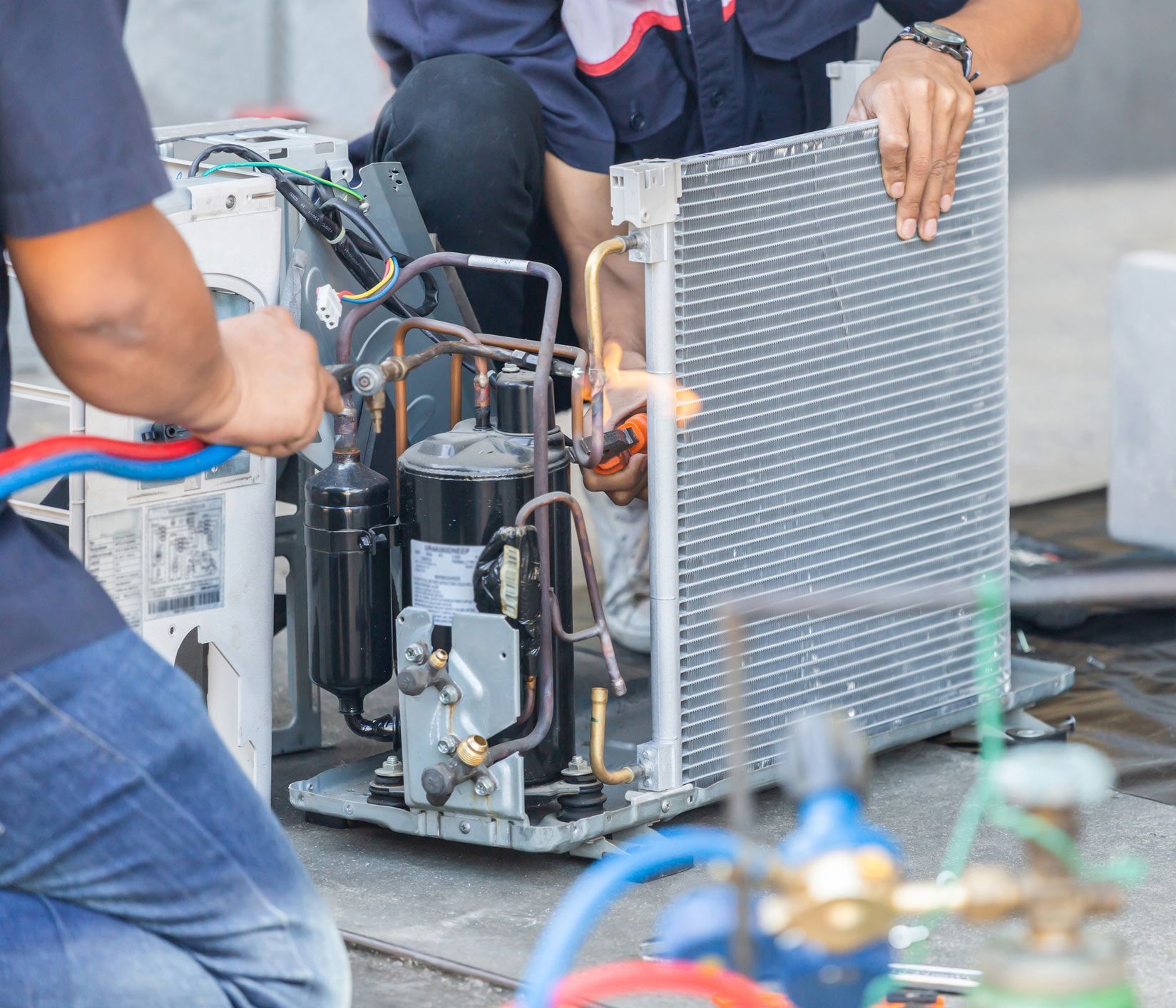 Two people repairing an air conditioner unit with tools.