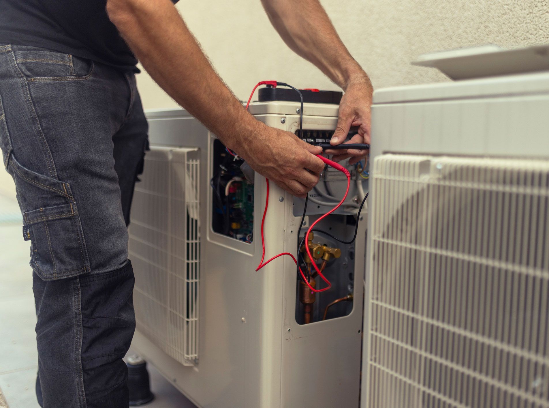 Person working on an AC unit, using tools and wires.