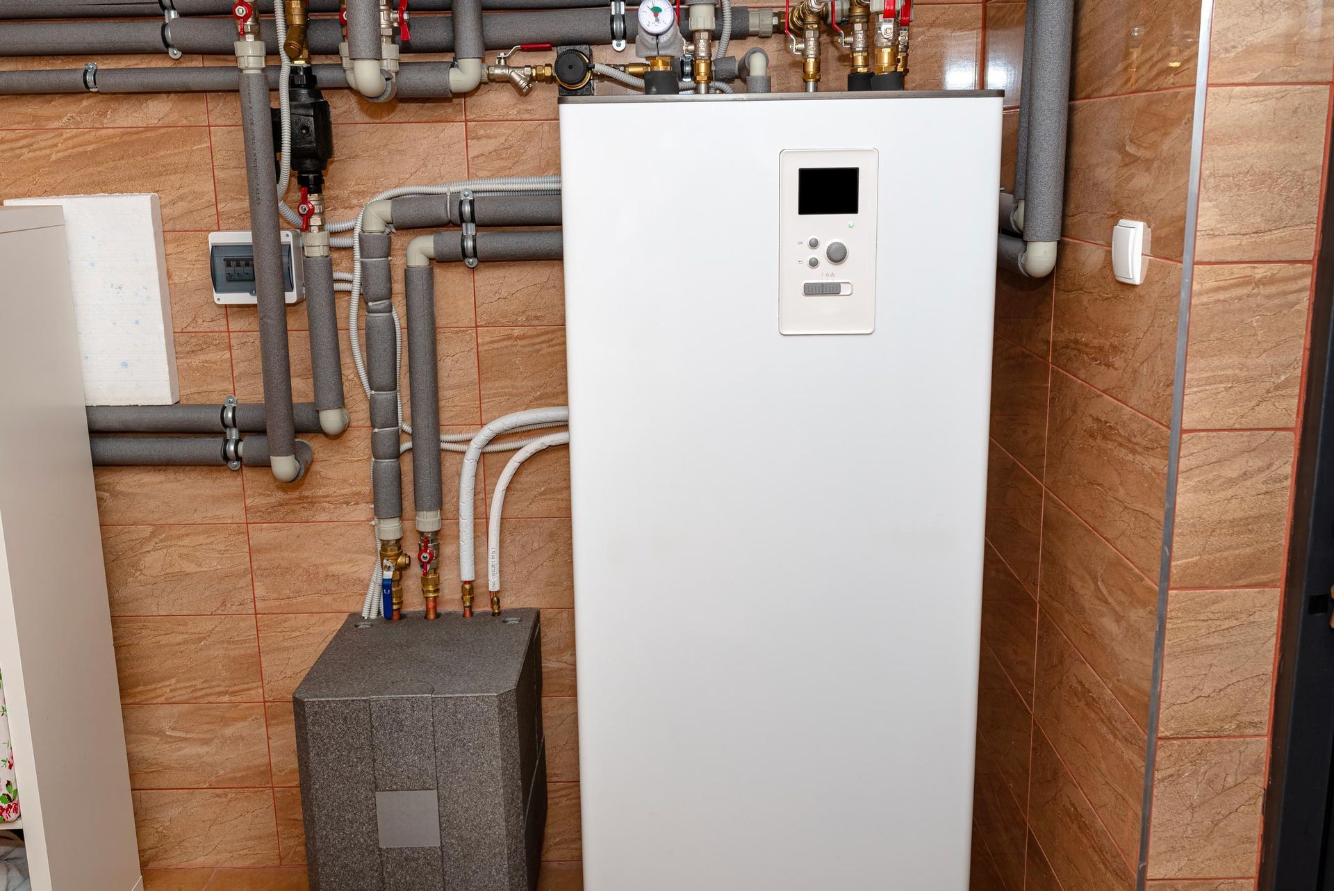 White water heater and insulated pipes on a tiled wall in a utility room.