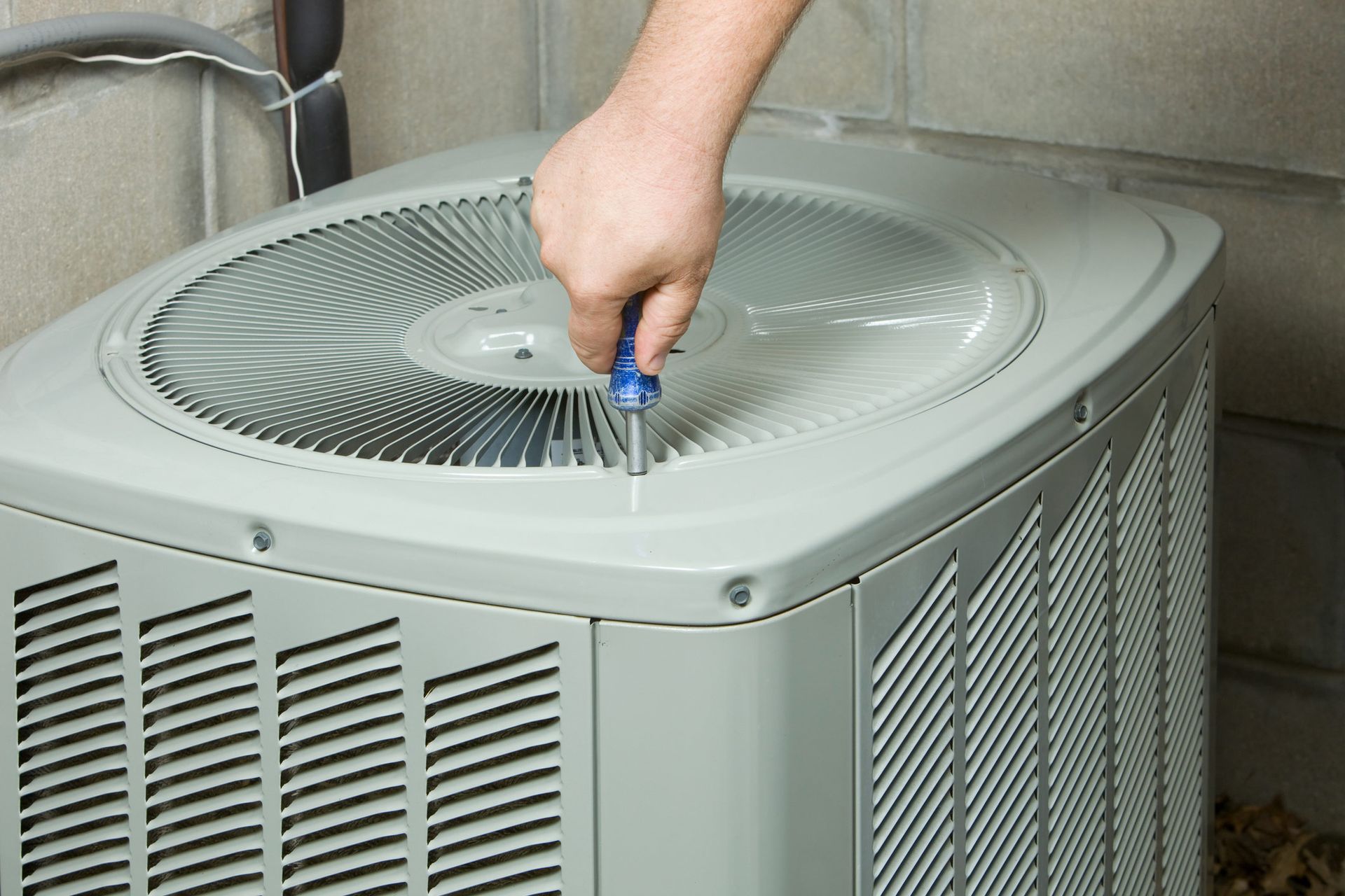 Person using a screwdriver to work on a central air conditioning unit outdoors.