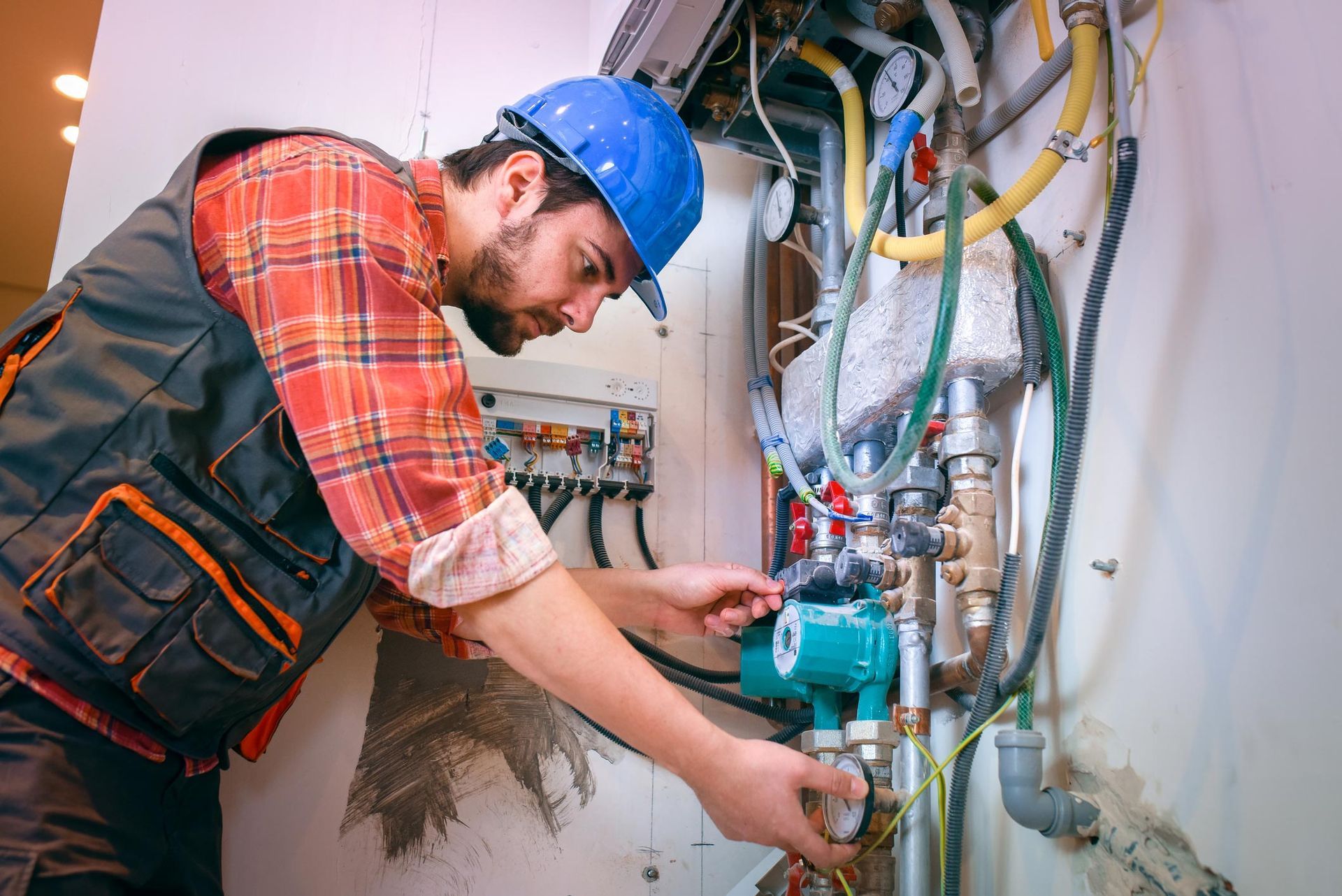 A technician in a blue hard hat inspects plumbing fixtures.