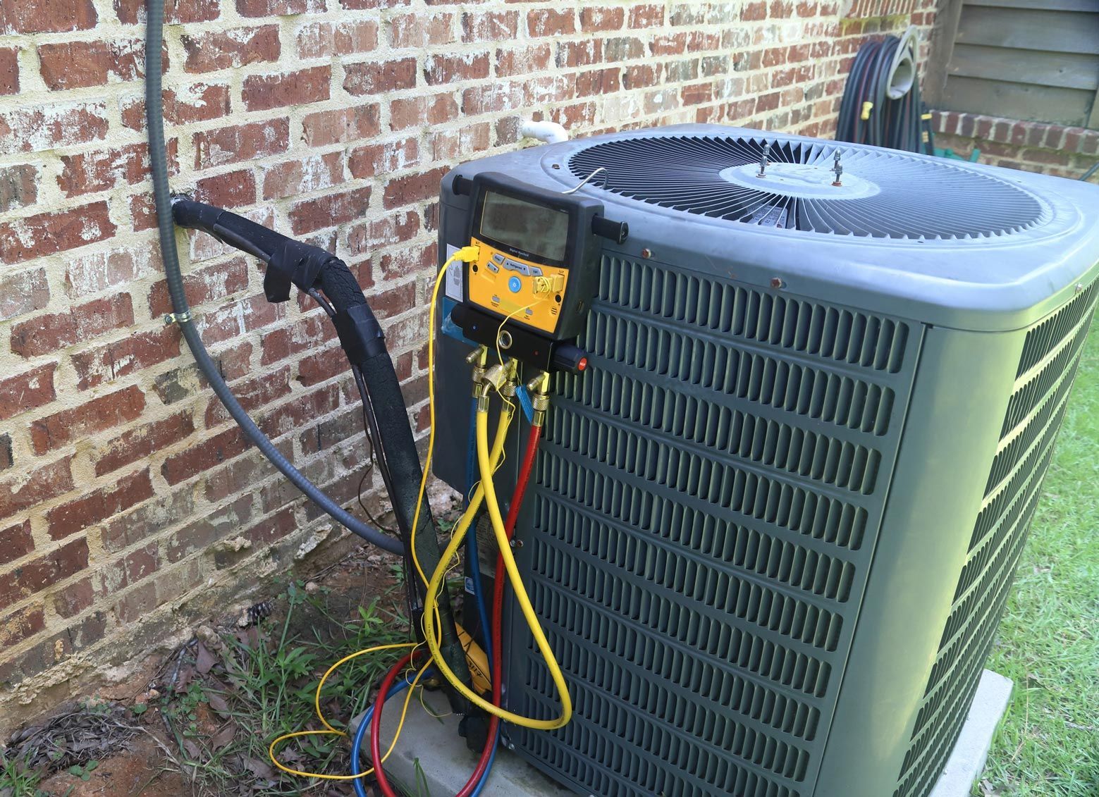 An air conditioning unit being serviced outdoors, with hoses and a gauge connected.
