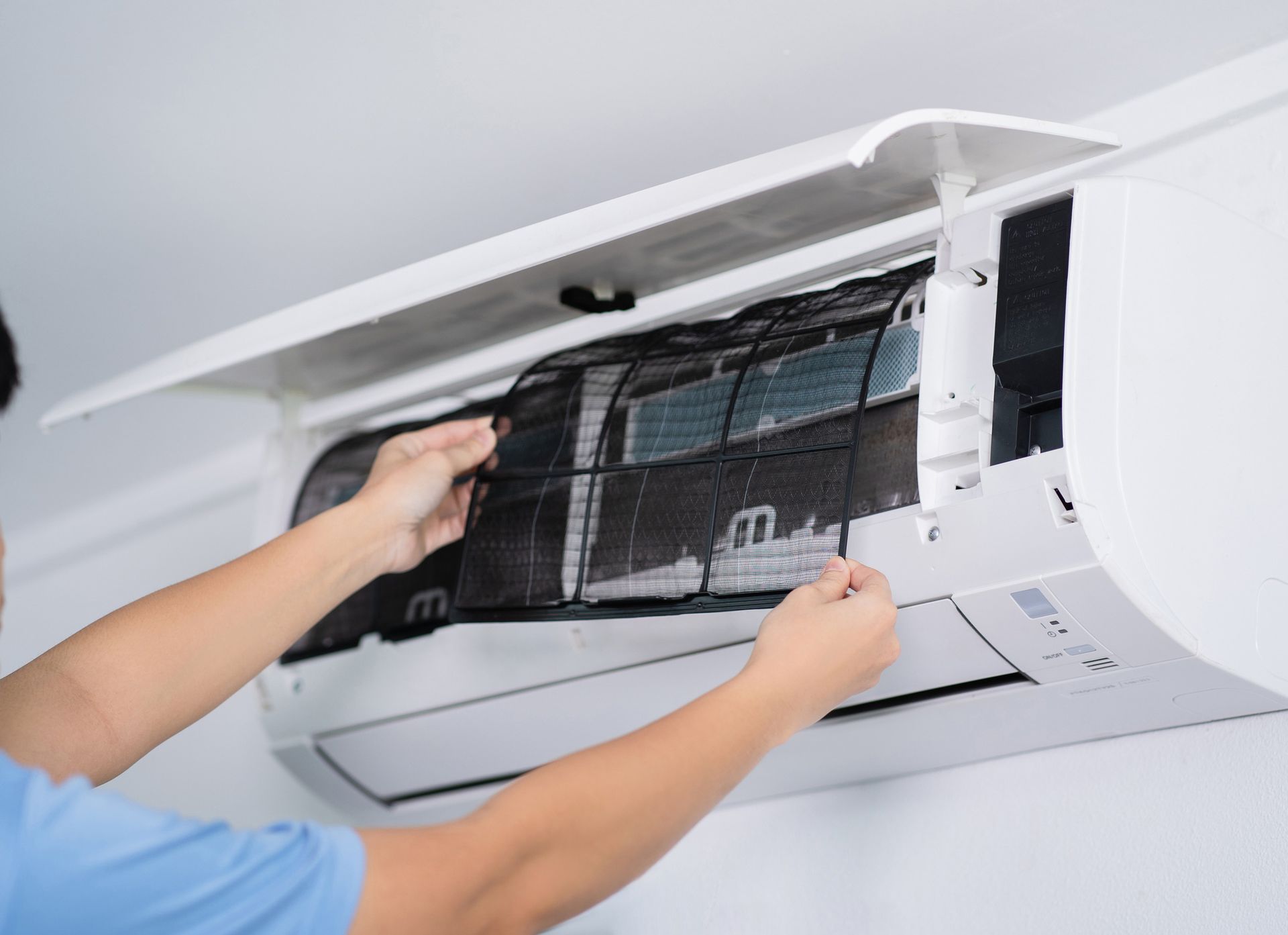 Person removing a dirty air filter from a white air conditioning unit on a white wall.