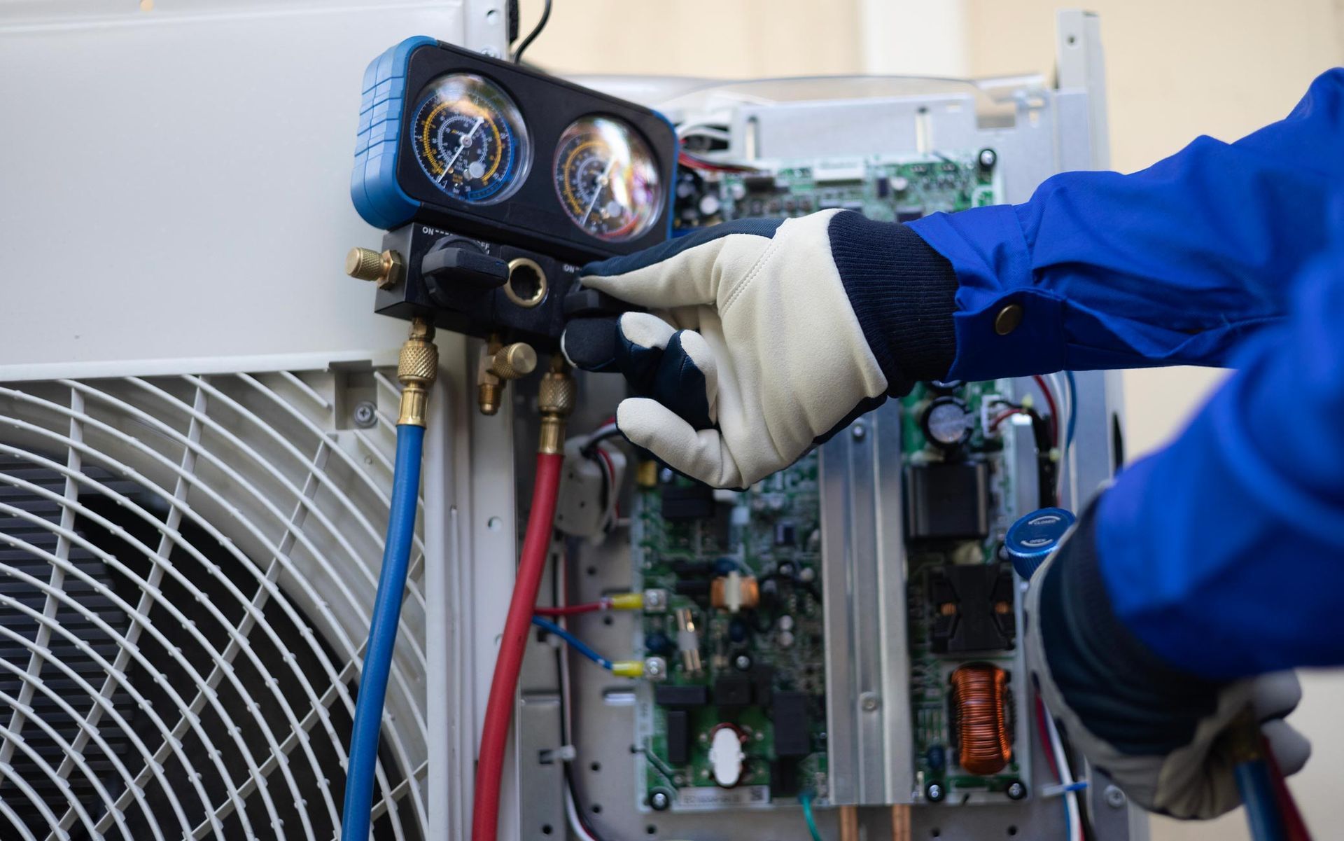 Mechanic wearing gloves, inspecting an air conditioning unit's gauges with hoses attached.