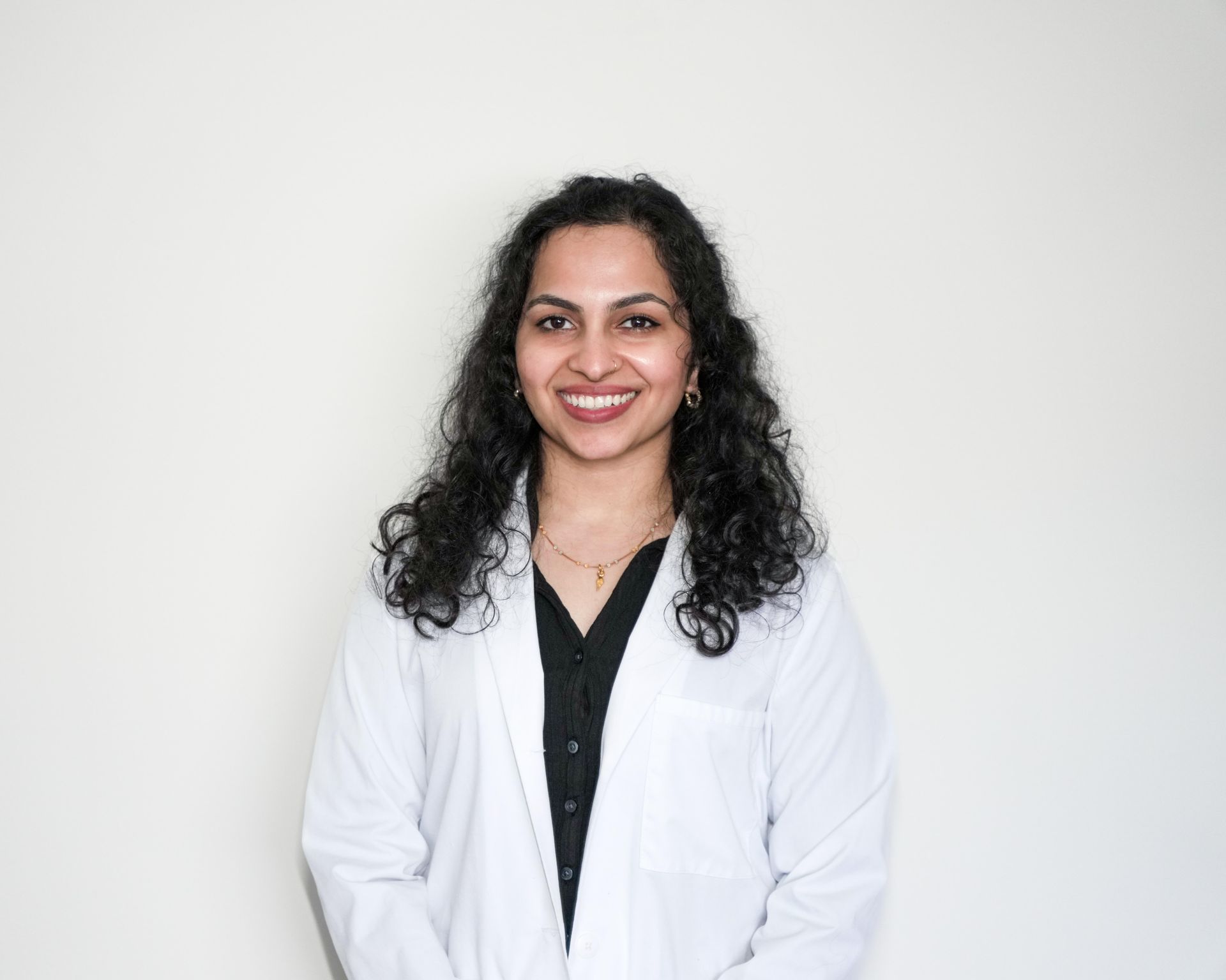 Smiling person in a white lab coat standing against a light gray background