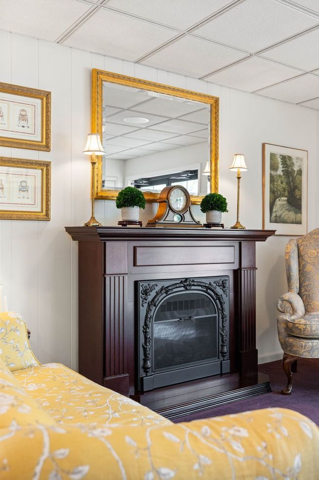Elegant room with dark fireplace, gold mirror, lamps, and yellow patterned chair