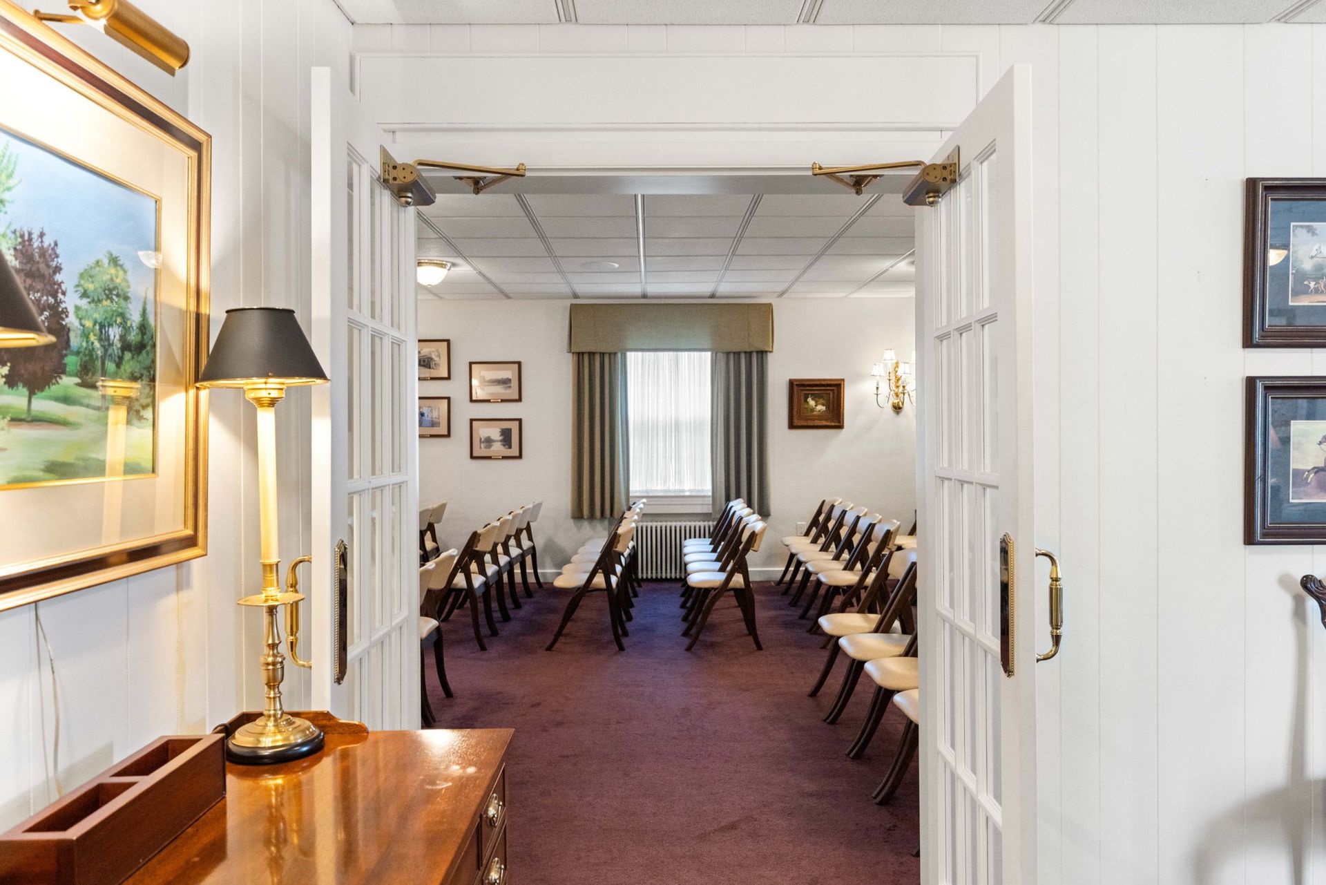 Elegant room with rows of chairs, framed art, and a doorway view to a curtained window