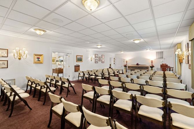 Empty room with rows of white chairs facing a casket