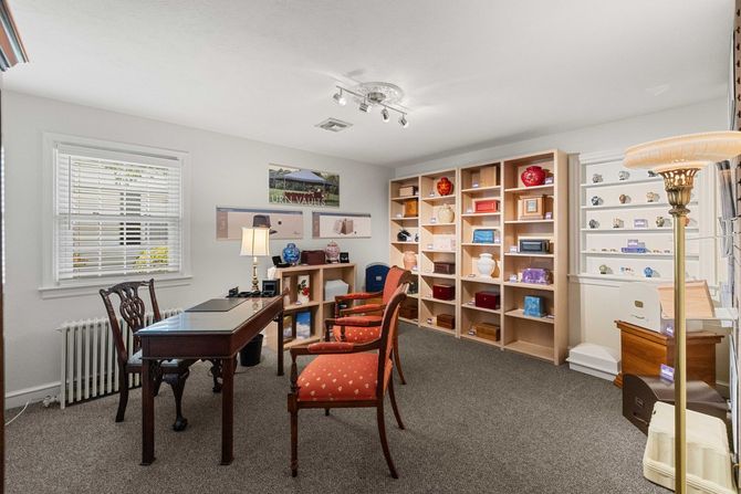 Home office with desk, chairs, bookshelves, and a window with blinds in a carpeted room
