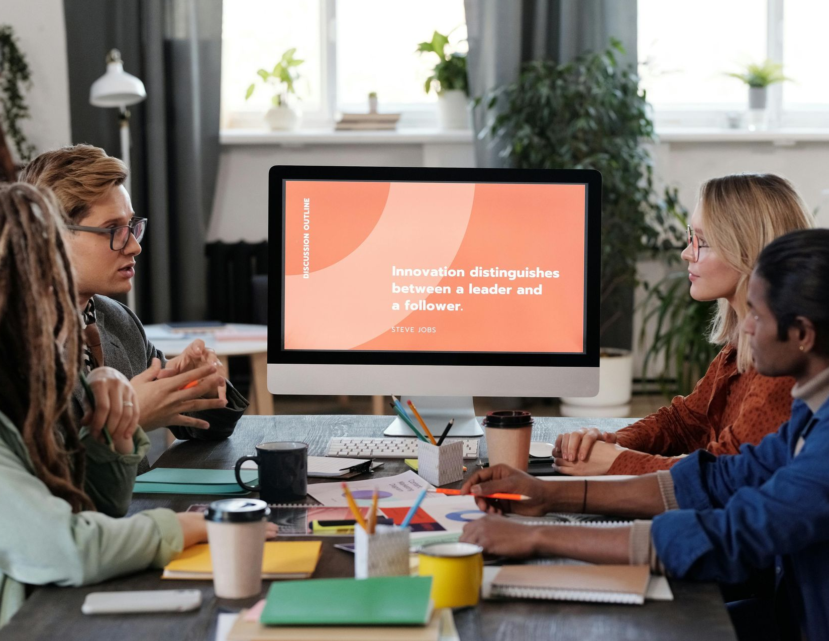 Group of people in a meeting, focused on a computer screen displaying a presentation.