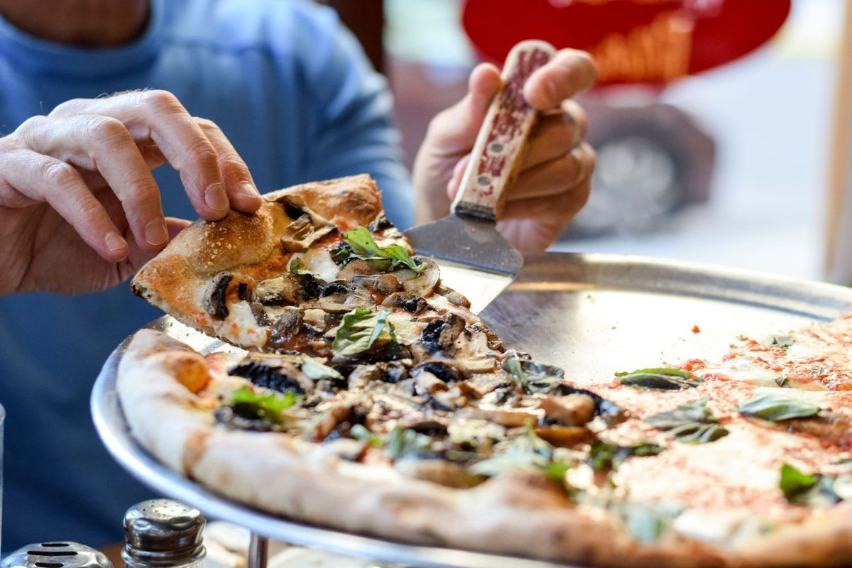 a person is taking a slice of pizza with a spatula .