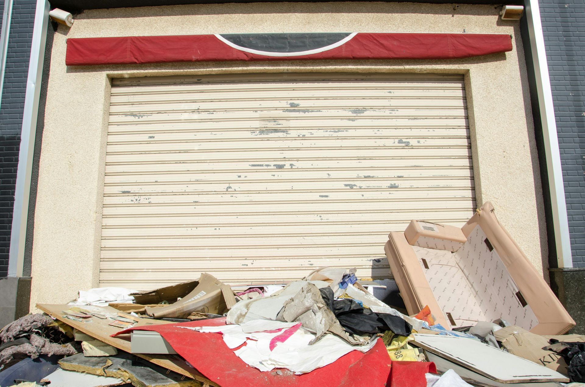 Closed storefront with a metal roll-up door; a pile of trash and debris is in front.