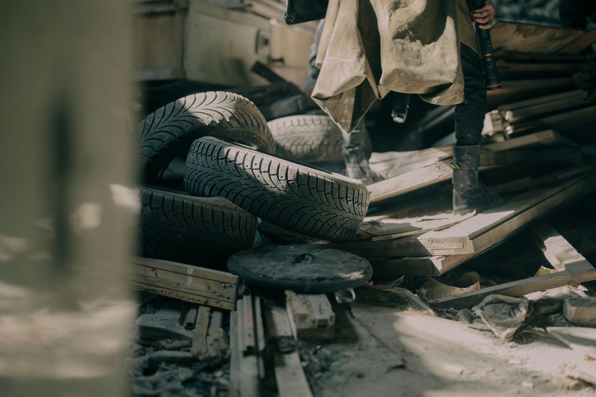 Pile of tires and wooden planks with a person in boots standing nearby, likely in a dilapidated outdoor setting.