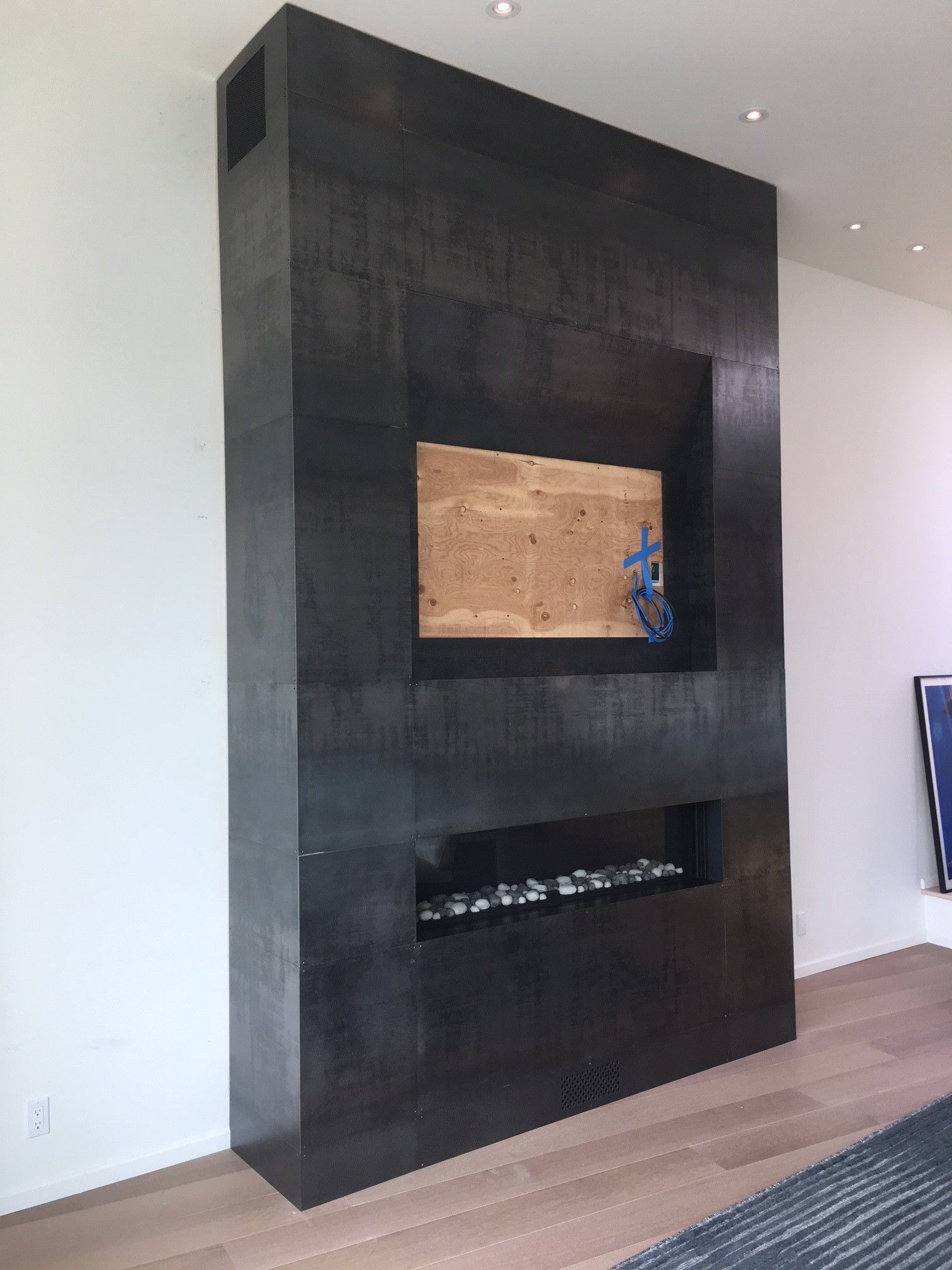 Dark gray fireplace built into white wall; has a square opening, and a firebox below.