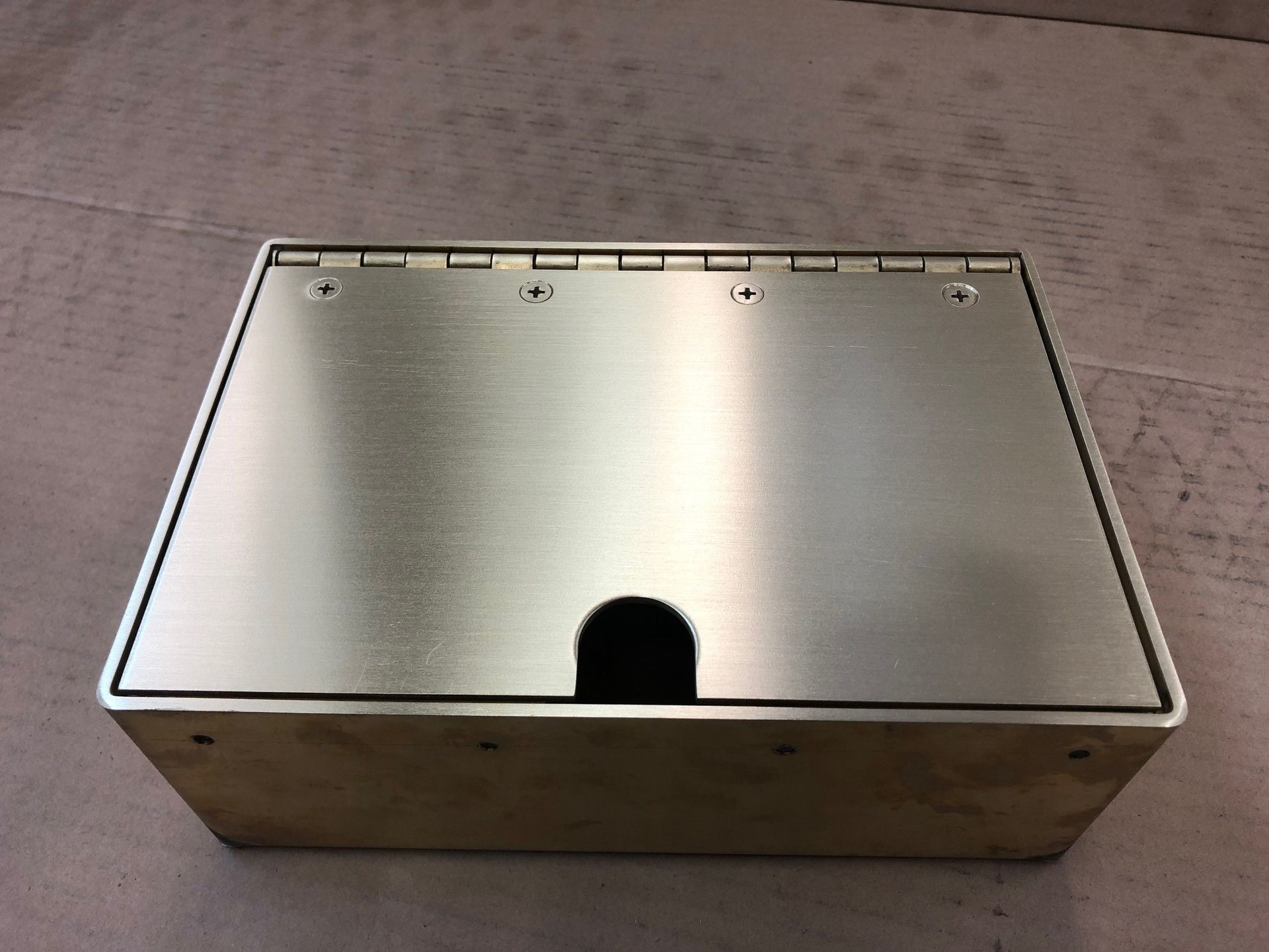 Brass-colored rectangular box with a hinged lid. The lid has a small, black, oval-shaped opening.