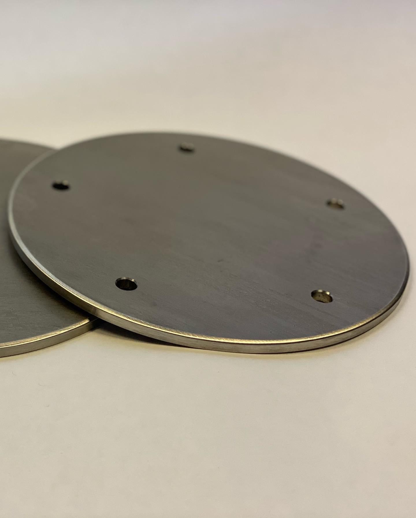 Two round metal plates with drilled holes, overlapping on a light background.
