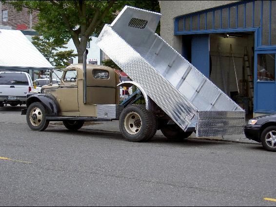 Tan vintage dump truck with aluminum bed raised on a city street.