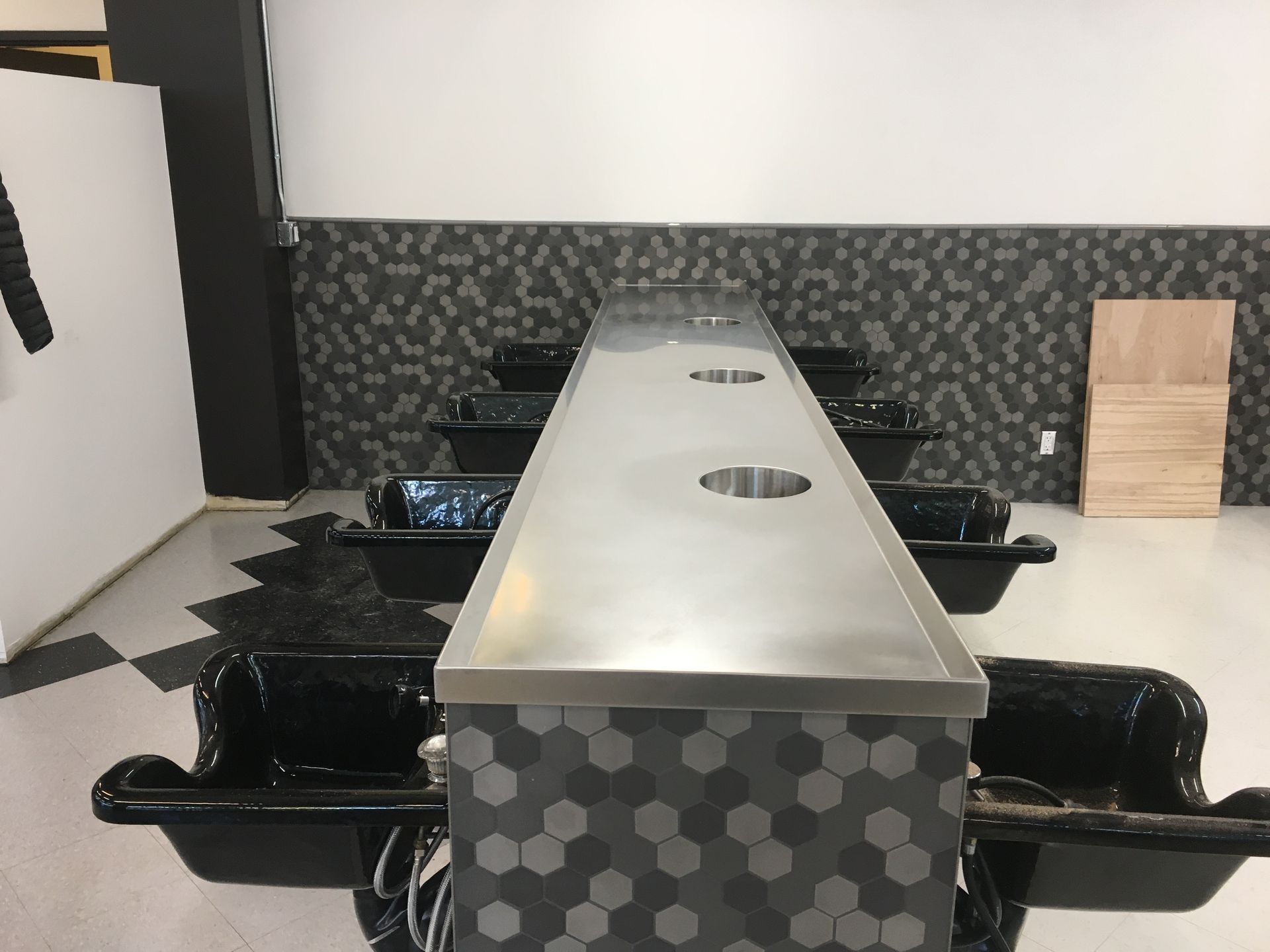 Salon with black basins and a stainless steel counter, accented with gray hexagon tiles.
