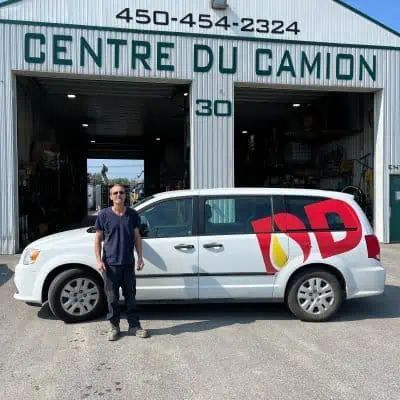 Un homme se tient à côté d'une camionnette blanche devant un immeuble.