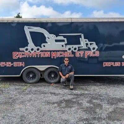 Un homme est agenouillé devant une roulotte qui indique excavation michel et fils.