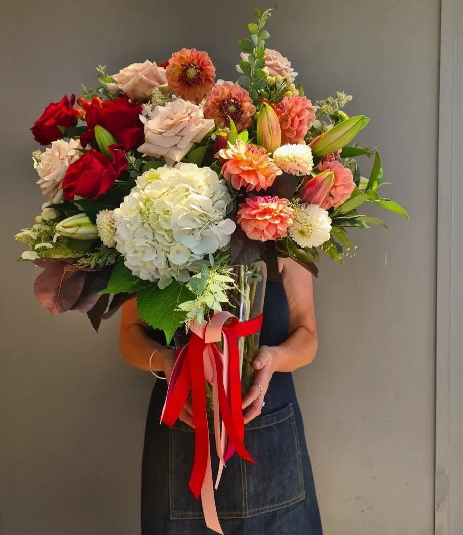 a woman is holding a vase of flowers with a red ribbon .