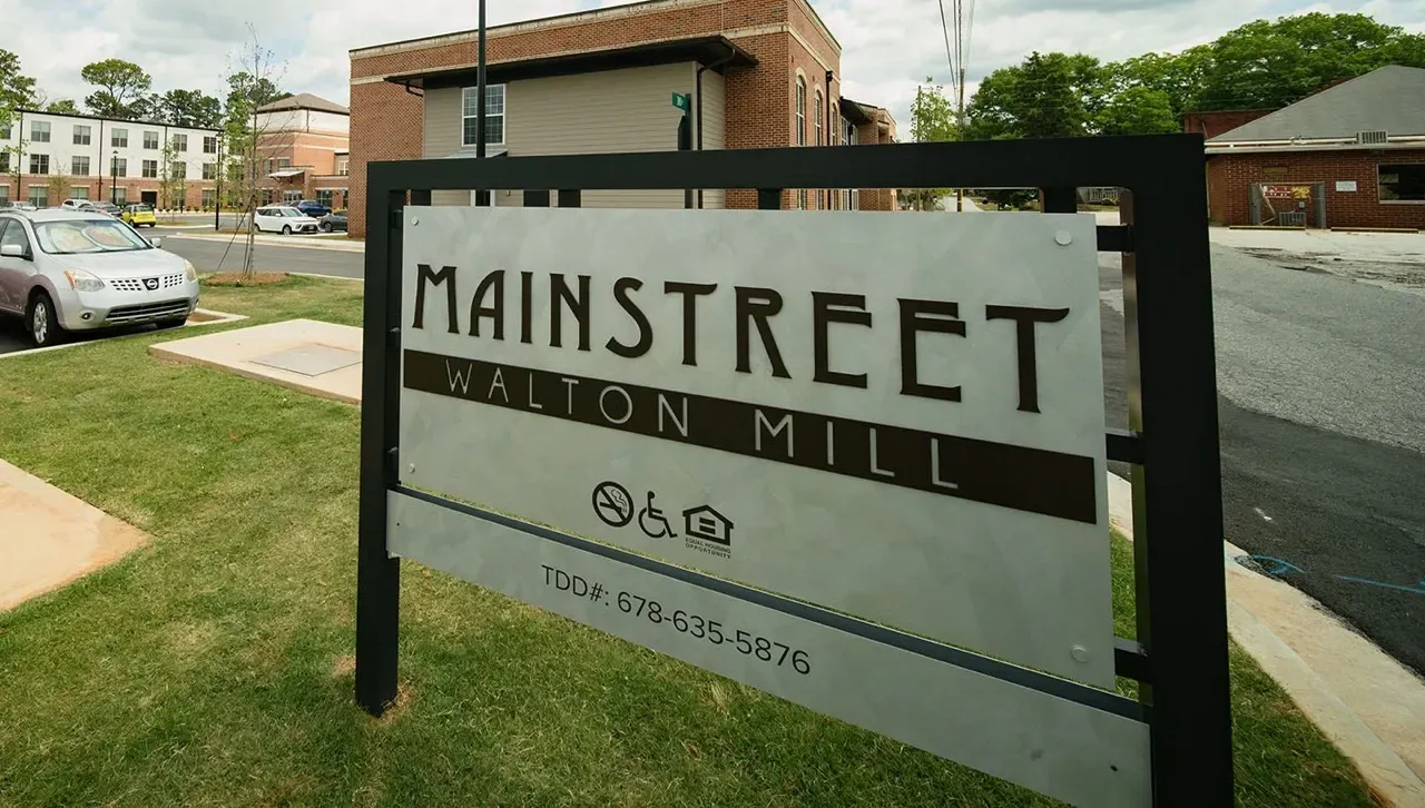 Exterior sign at the Mainstreet Walton Mill entrance with surrounding buildings.