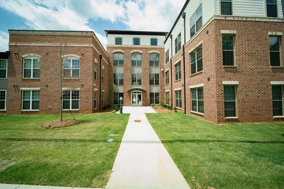 Exterior view of brick apartment buildings with a central walkway to the entrance.