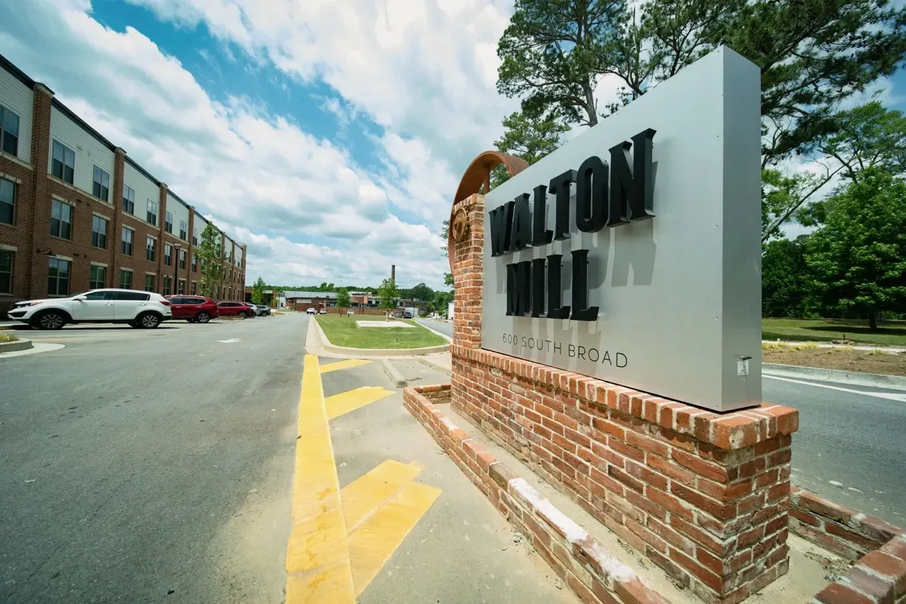 Exterior view of Walton Mill apartment community entrance with brick monument sign and parked cars.