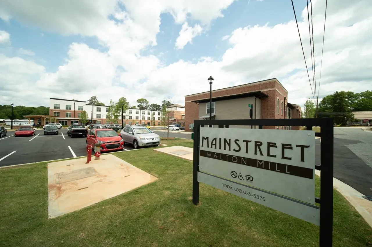 Exterior view of the Main Street Walton Mill apartment community with a large sign and parking lot.