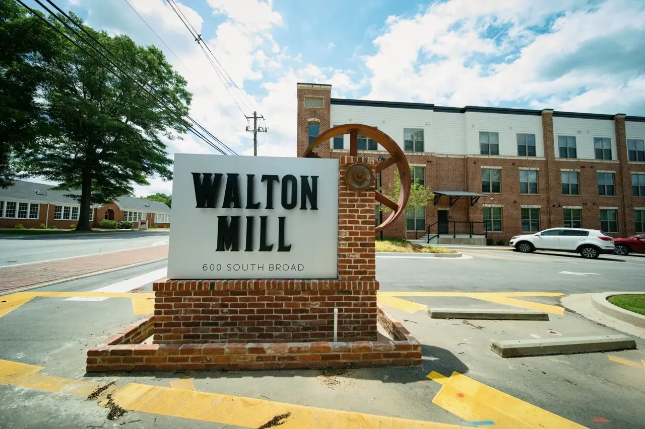 Exterior sign for Walton Mill with brick building in the background.