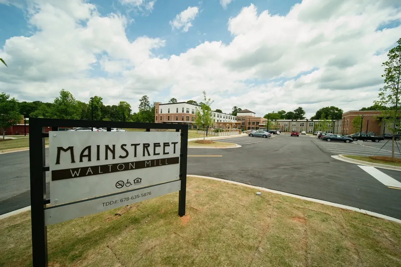 Exterior sign for Mainstreet Walton Mill with a parking lot and buildings in the background.