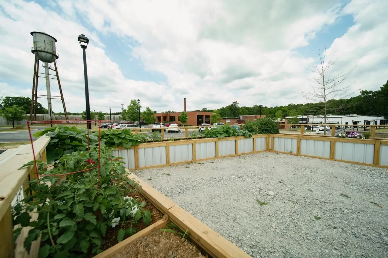 Exterior community courtyard with gravel lot, wooden planters, and a water tower in the background.